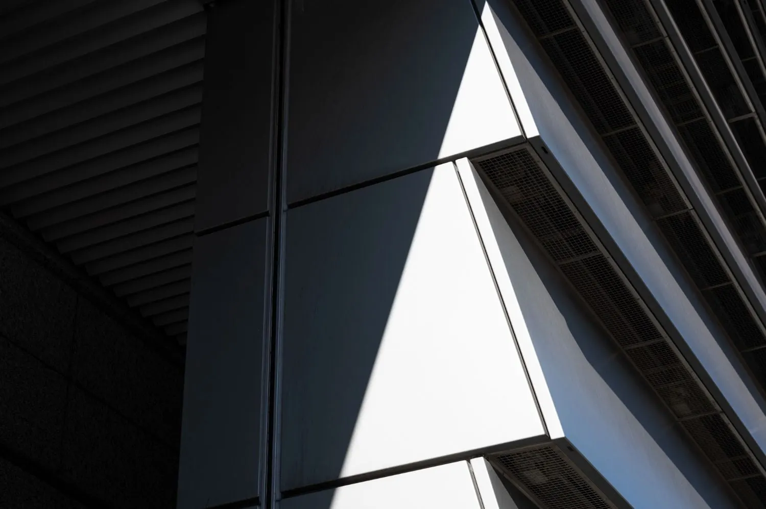 Nahaufnahme einer modernen Gebäudeecke mit geometrischen Paneelen und kontrastreichen Schatten.