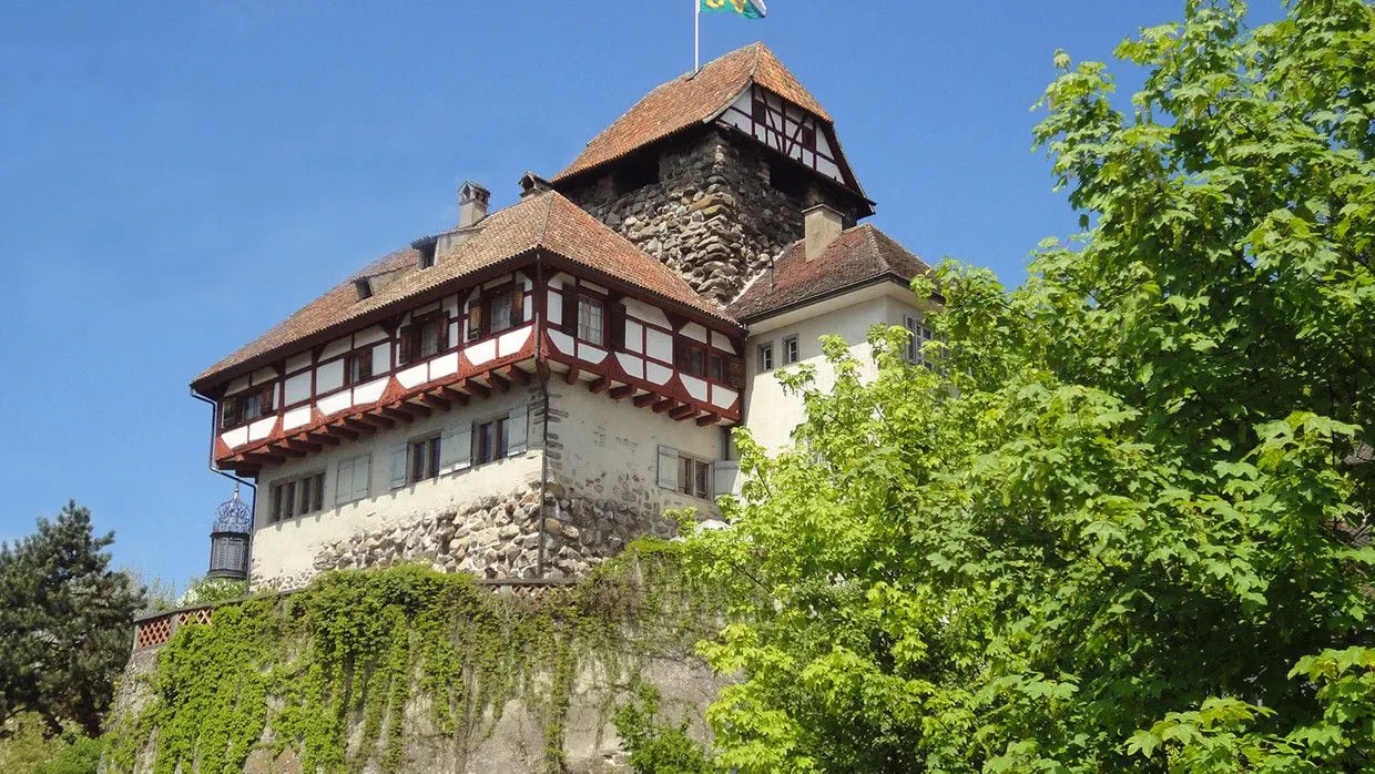 Auf einem Hügel steht ein grosses Gebäude, umgeben von Bäumen.